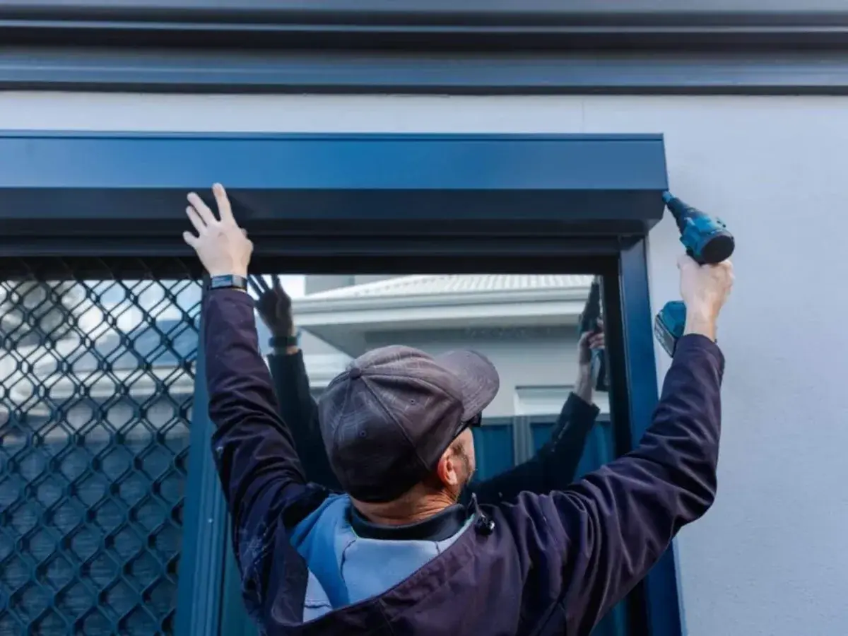 Technicien fixant le coffre d'un volet roulant sur une façade à Auderghem